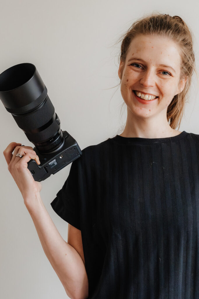 Fotografin mit Kamera in der Hand, lacht in die Kamera