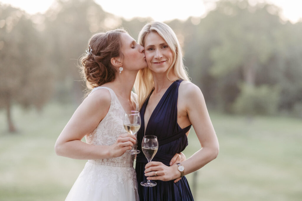 Braut ud Trauzeugin (ihre Schwester) mit Kuss auf die Wange im Abendlicht