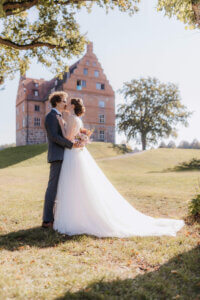 Brautpaar beim Paarshooting im Sonnenschein, küsst sich innig vor Schloss Ulrichshusen