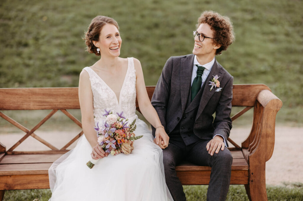 Brautpaar lachend auf einer Bank beim Paarshooting mit der Hochzeitsfotografin Mecklenburg