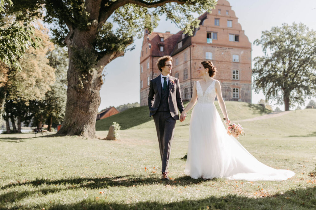 Brautpaar läuft Hand in Hand vor dem Schloss und Gut Ulrichshusen