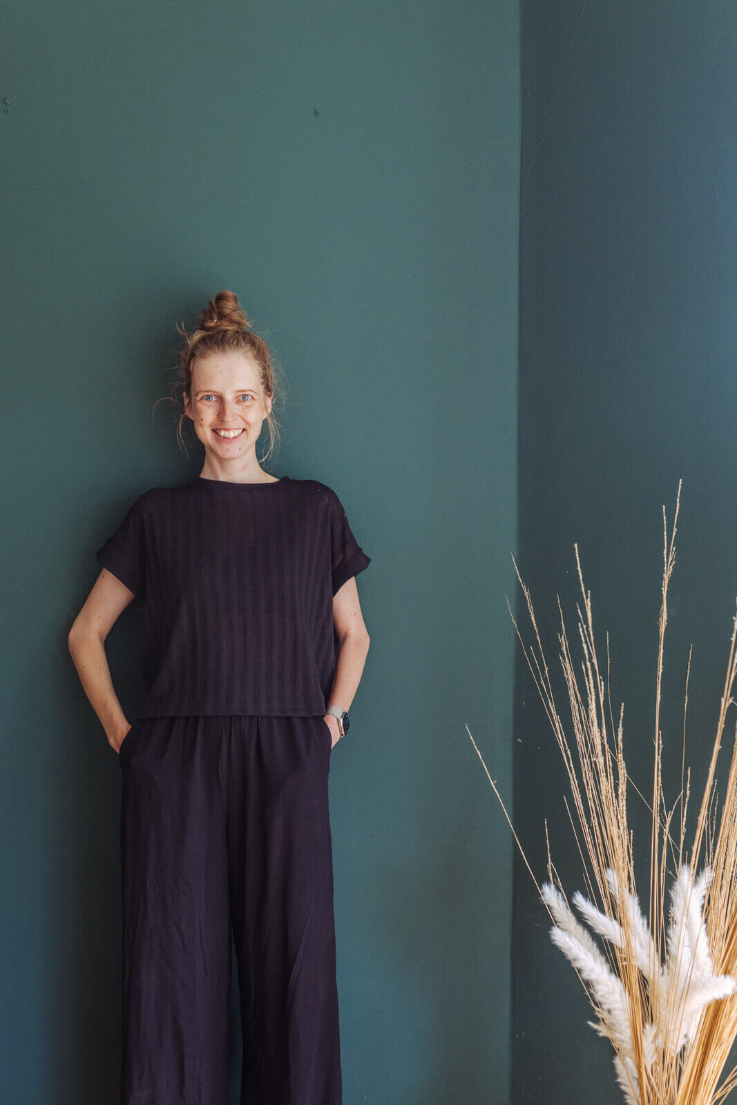 Fotografin Selbstporträit schaut in die Kamera und lacht, steht vor grüner Wand, indoor