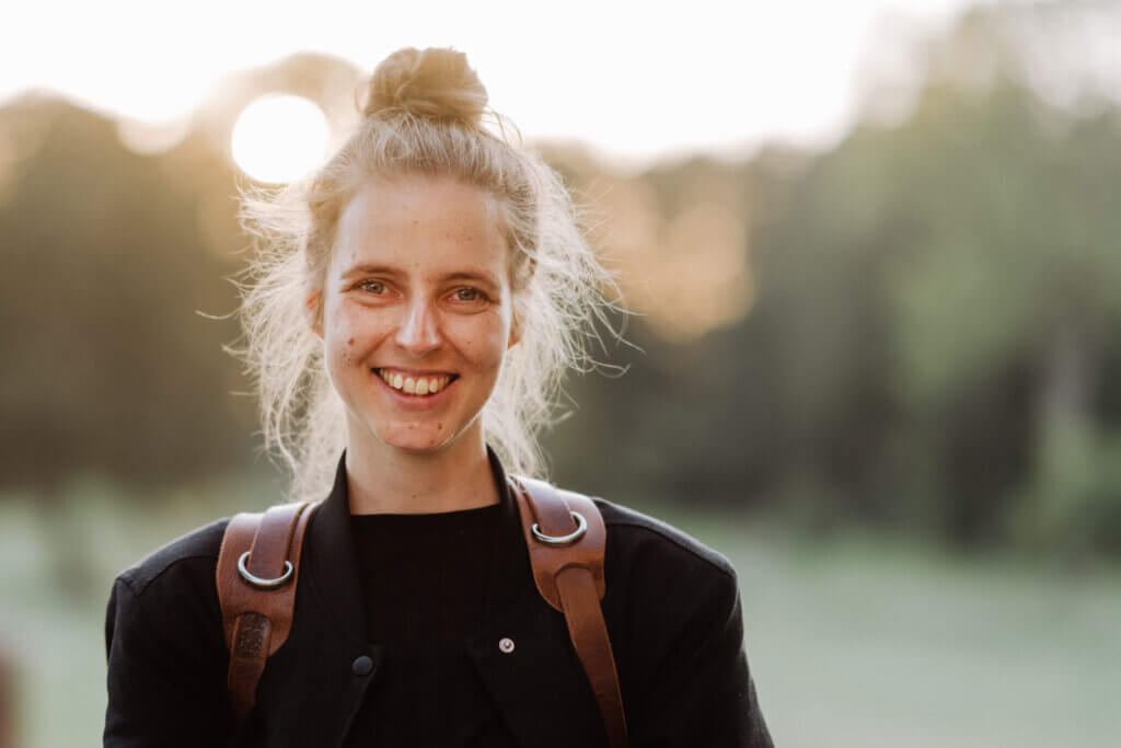 Hochzeitsfotografin am Tag einer Hochzeitsreportage im Sonnenuntergang, schaut lachend in die Kamera