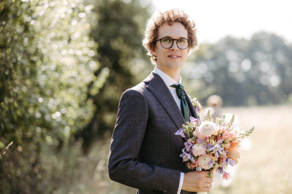 Der Bräutigam mit dem Brautstrauß in der Hand im Sonnenlicht