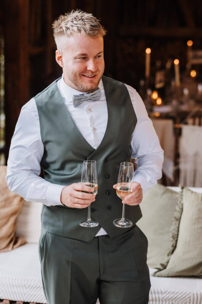 Bräutigam locker mit Sektgläsern in der Hand, Feldscheune Schöbendorf