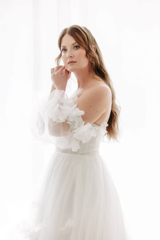 Braut beim Getting Ready vor einem hellen Fenster beim Anlegen der Ohrringe