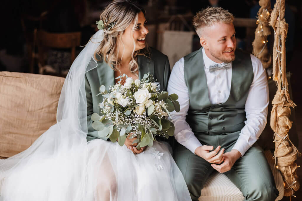 Braut und Bräutigam sitzen locker auf einer großen Schaukel in der Feldscheune Schöbendorf