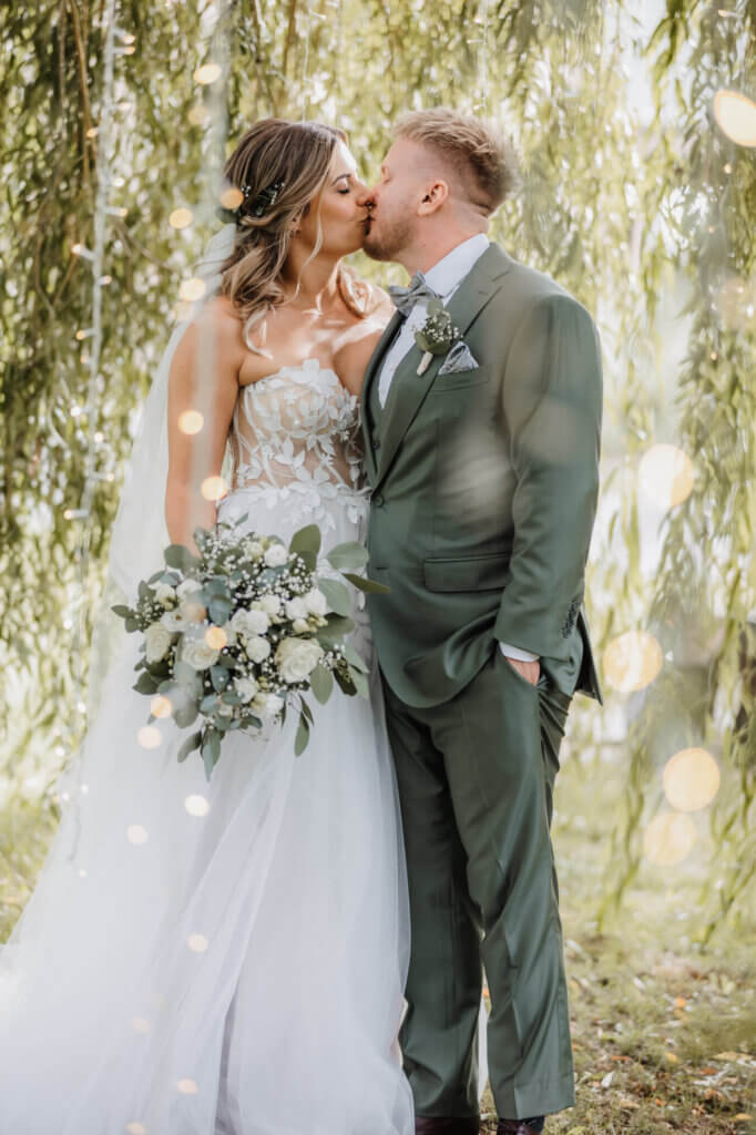 Das Brautpaar küsst sich unter der Trauerweise mit LIchtinstallationen