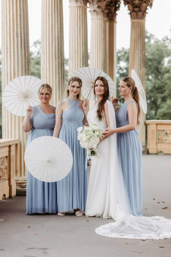 Braut mit ihren farblichen passend gekleideten Brautjungfern und weißen Schirmen im Säulengang vom Belvedere Pfingstberg