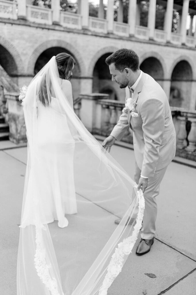 Bräutigam richtet die Schleppe seiner Braut beim First Look Shooting