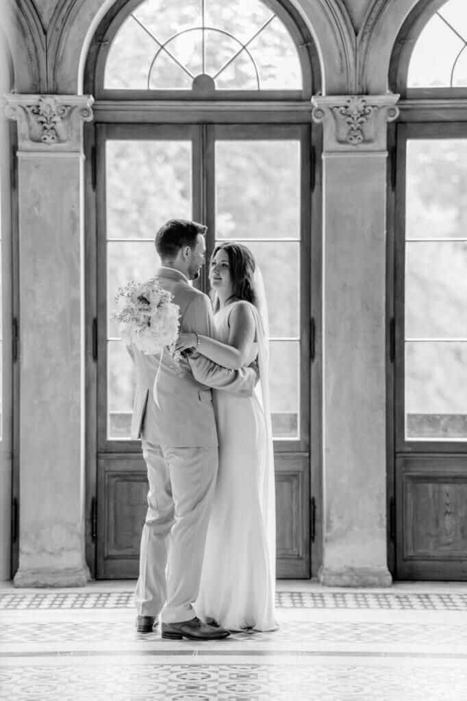 Das Brautpaar tanzt vor großen Fenstern