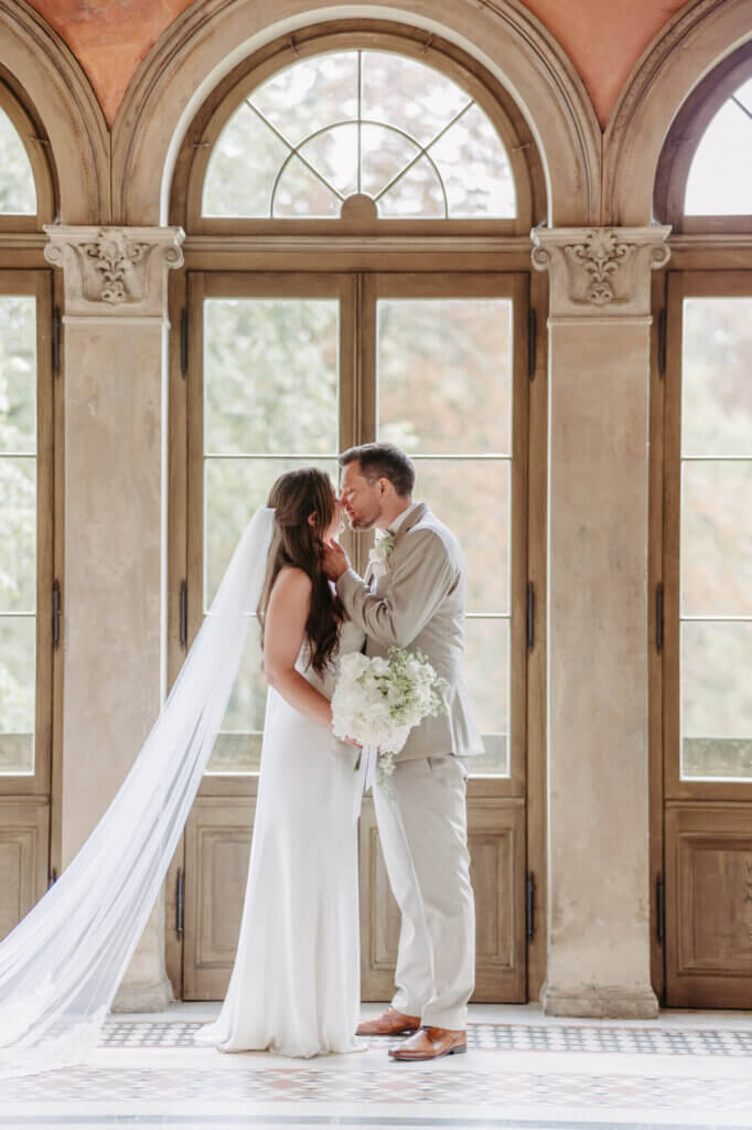 Ein zarter Kuss vor großen Fenstern, festgehalten von der Hochzeitsfotografin Potsdam