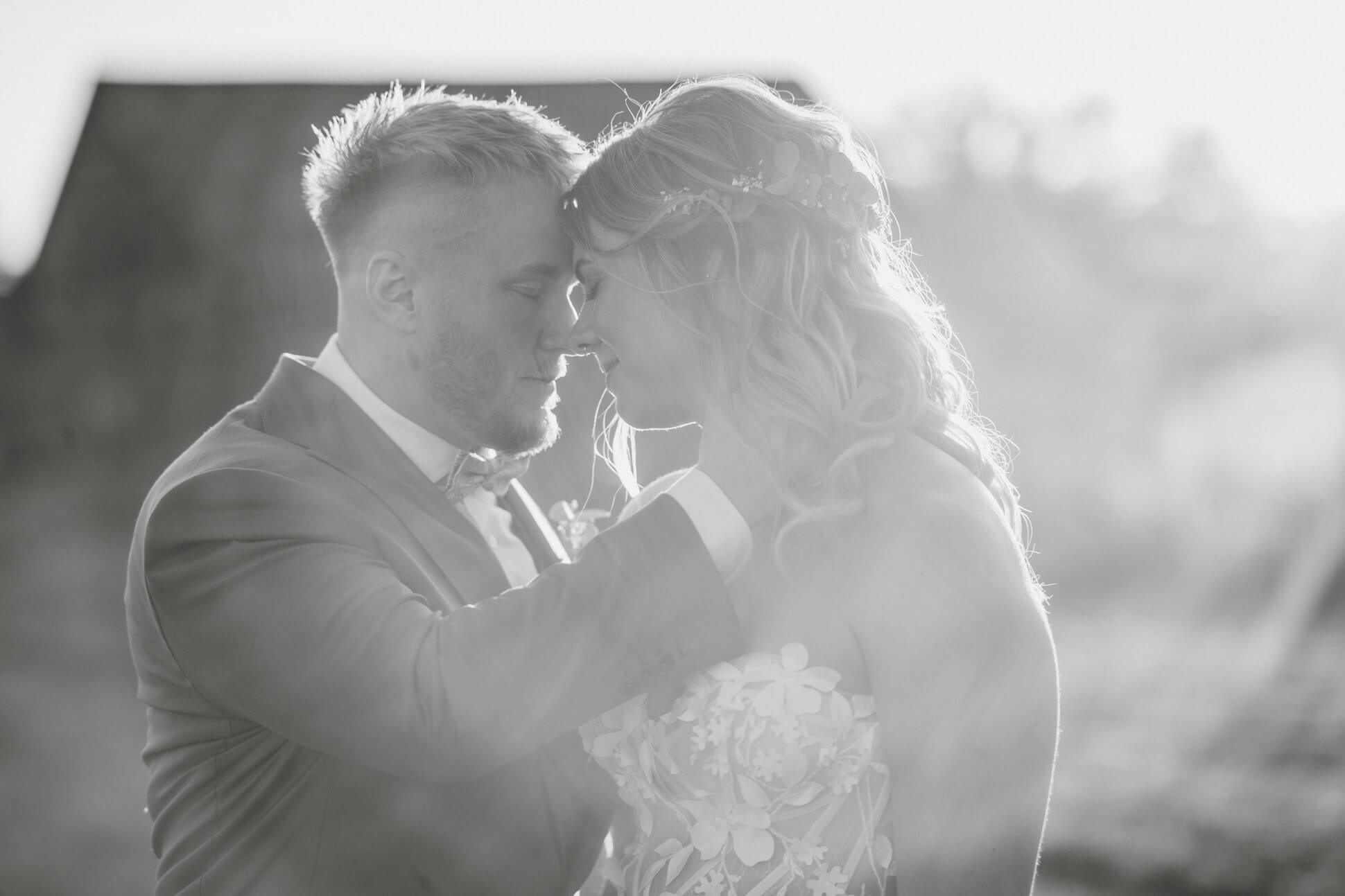 Brautpaar steht in inniger Umarmung im Abendlicht schwarz weiß Feldscheune Schöbendorf in Brandenburg