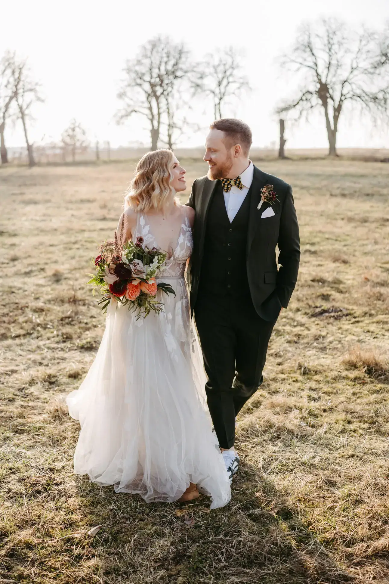 Brautpaar läuft entspannt über ein Feld in Brandenburg und lächelt sich an